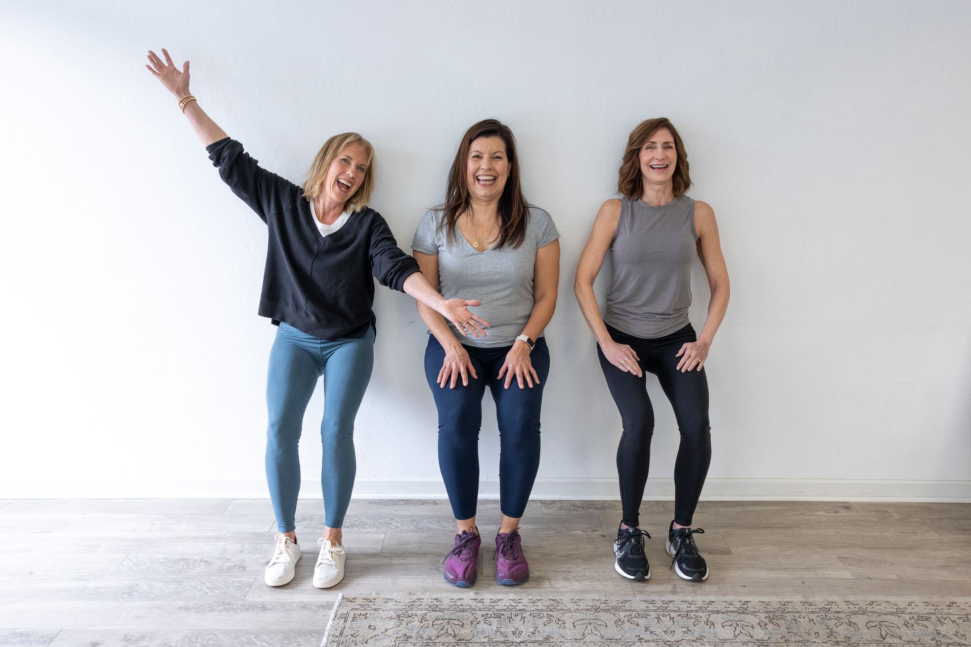 Three women are standing next to each other in front of a white wall.