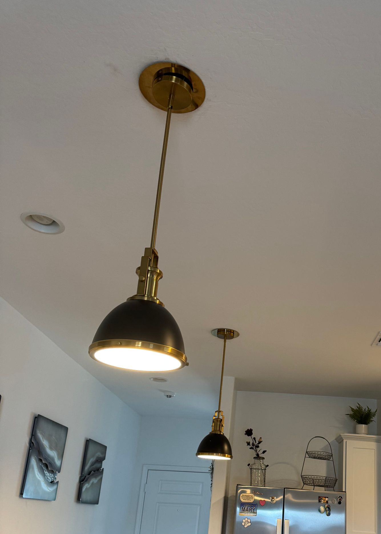 Two pendant lights with black domes and brass accents hang from a white ceiling.