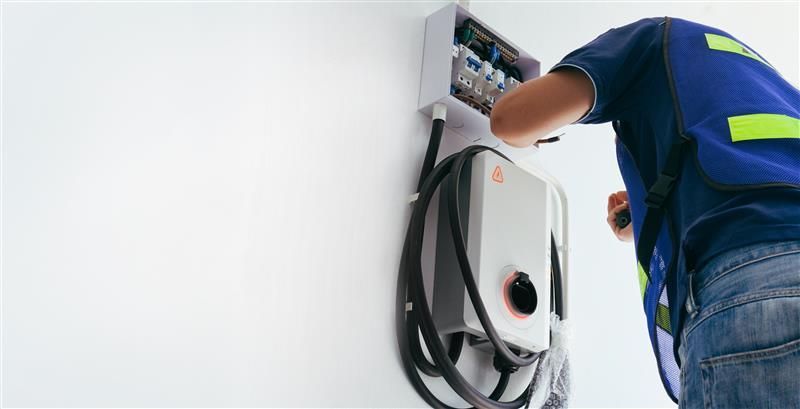 Electrician installing EV charger on a white wall.