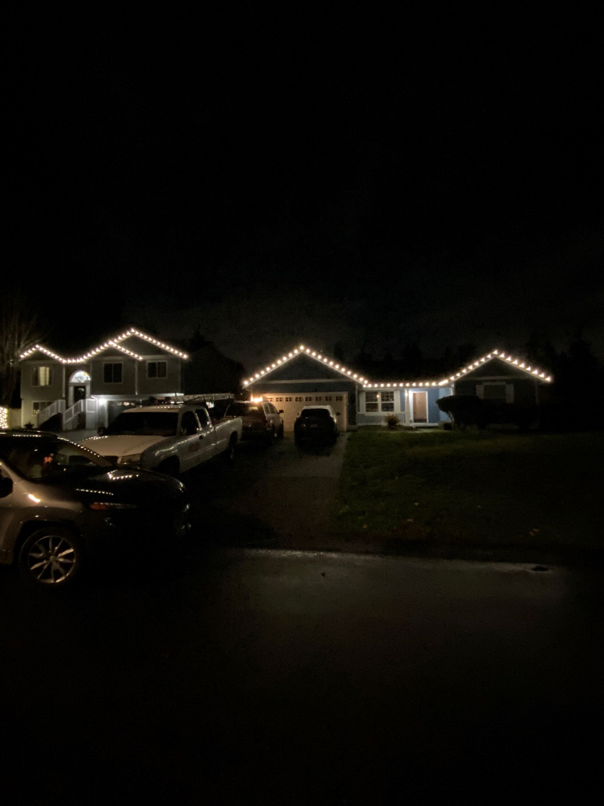 A house with christmas lights on the roof is lit up at night.