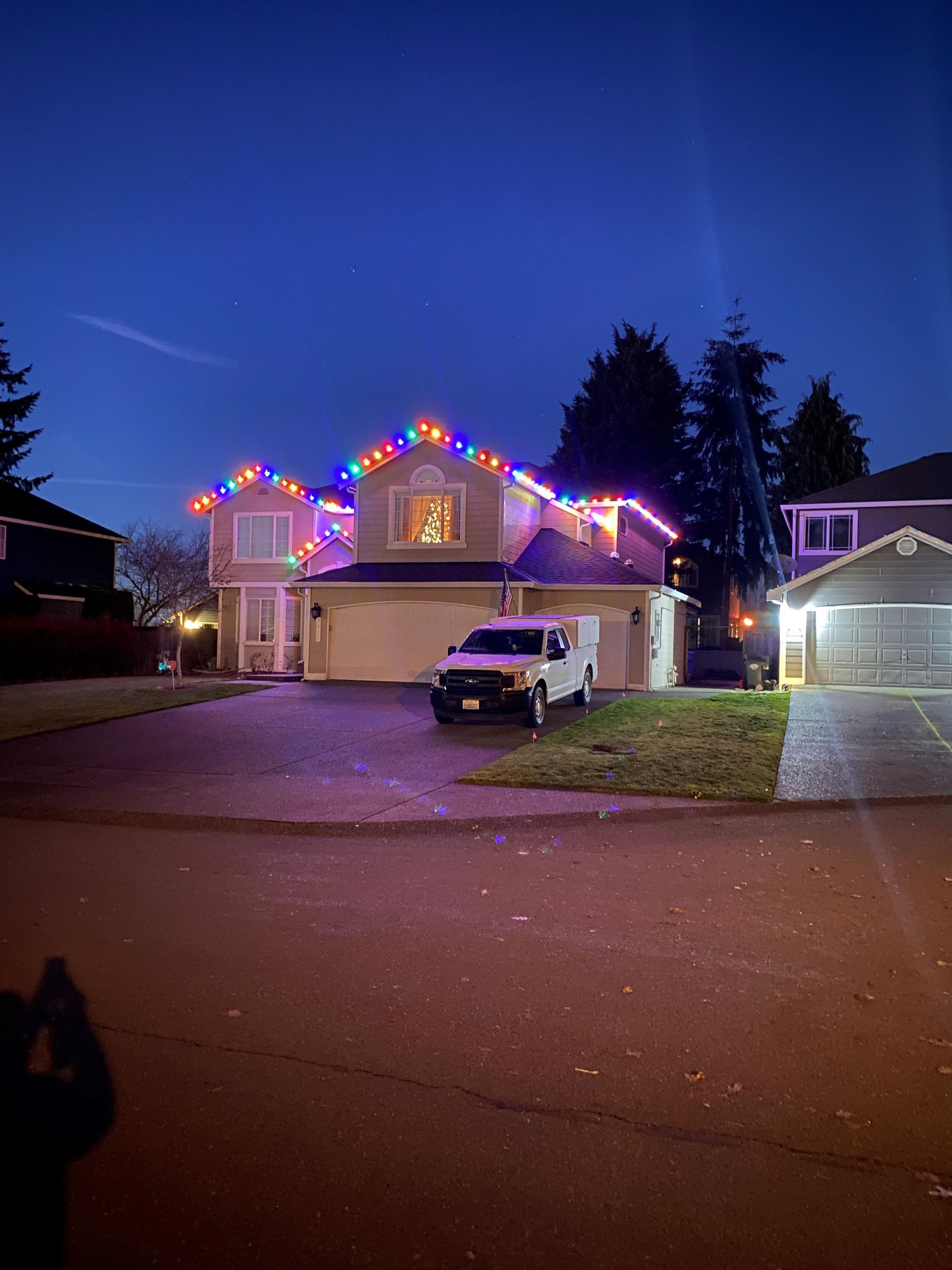 A white van is parked in front of a house decorated with christmas lights.