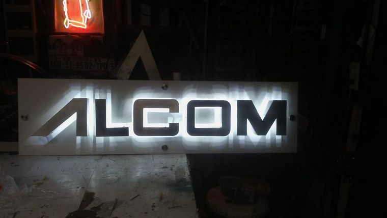 A sign that says alcom is lit up at night.