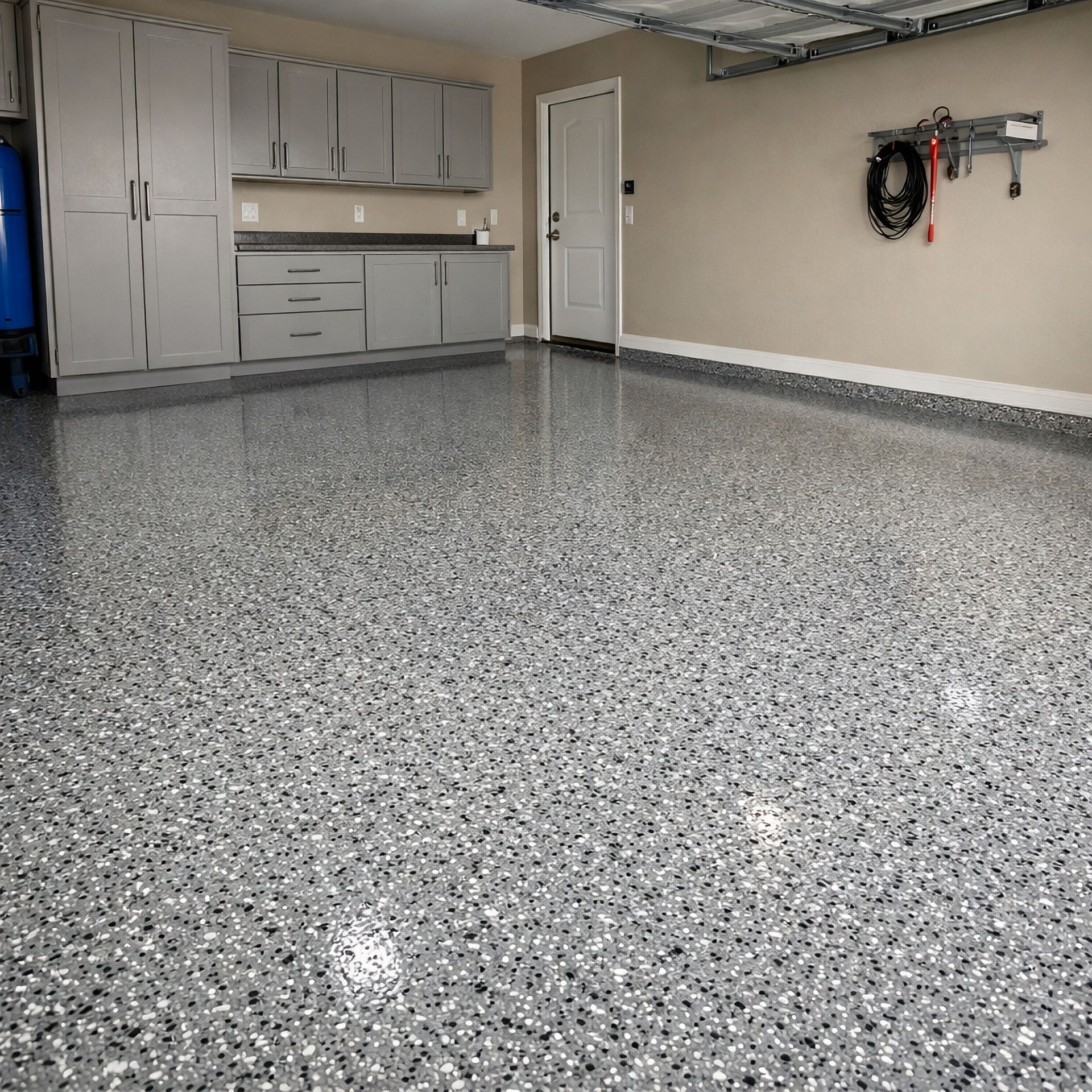 Empty garage with speckled epoxy floor, cabinets, and wall-mounted tools.