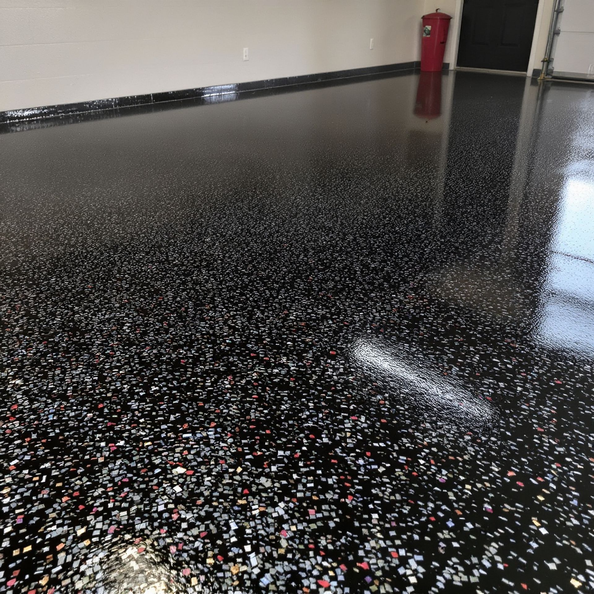 Glossy black speckled epoxy floor in an empty room with a red fire extinguisher on the wall