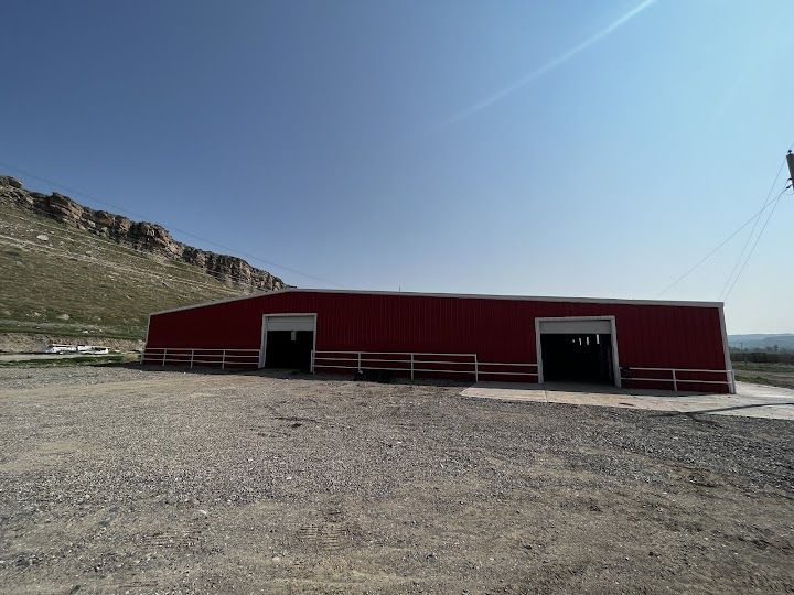 A large red barn is sitting in the middle of a dirt field.