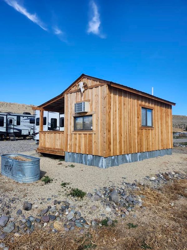A small wooden cabin is sitting in the middle of a dirt field.