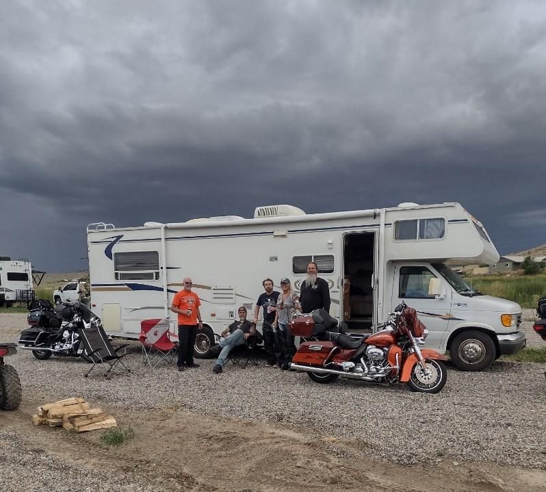 A group of people standing in front of a rv and motorcycles
