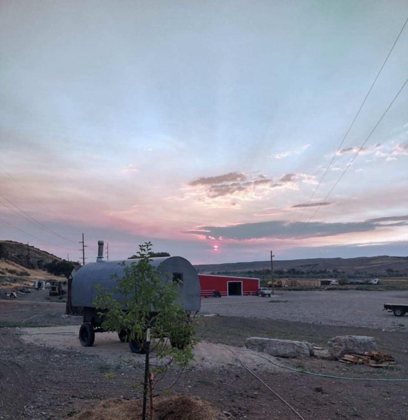 A large tank is parked in a dirt field at sunset.