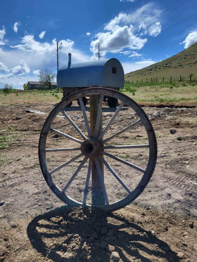 A mailbox is attached to a wagon wheel in a dirt field.