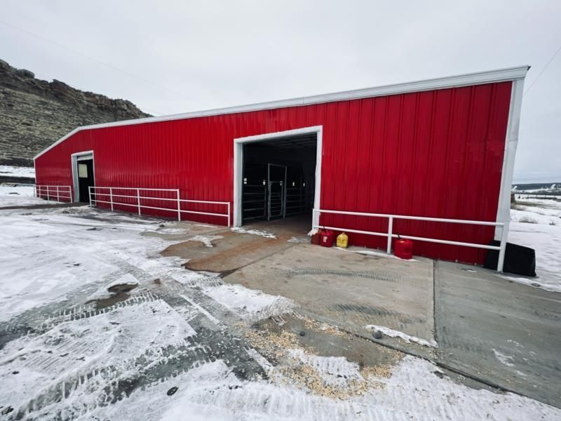 A large red barn is sitting in the middle of a snowy field.