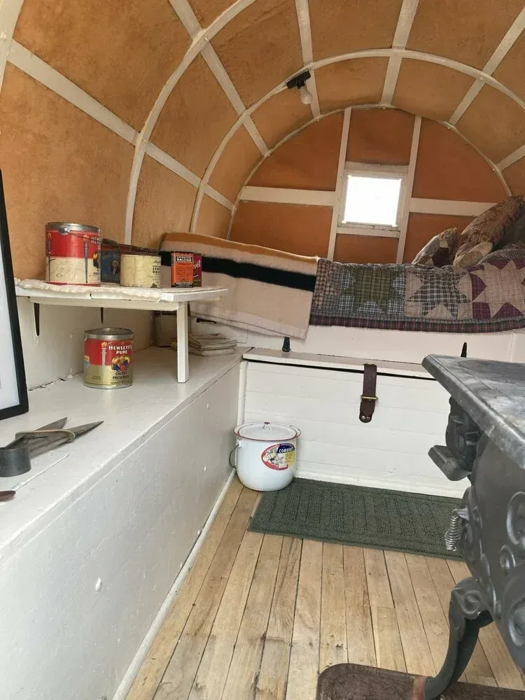 The inside of a wagon with a bed and a pot on the floor.