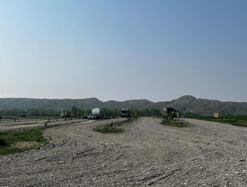 A dirt road with mountains in the background and cars parked on the side of it.