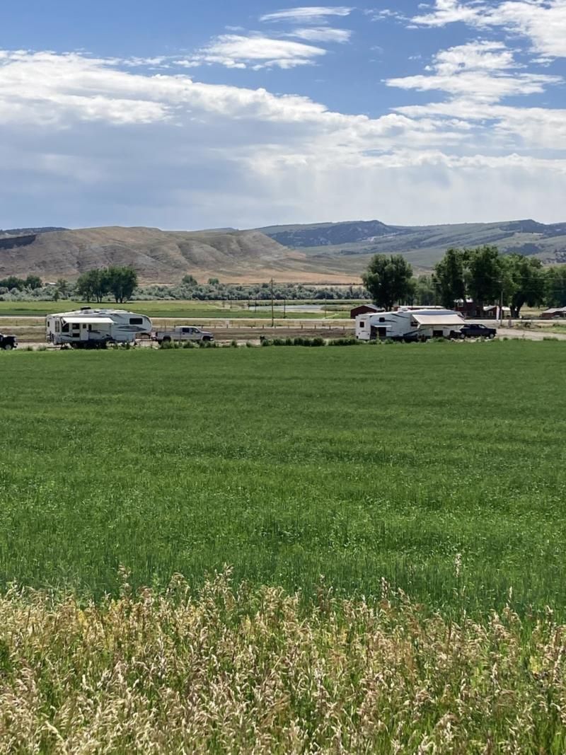 A row of rvs are parked in a grassy field with mountains in the background.