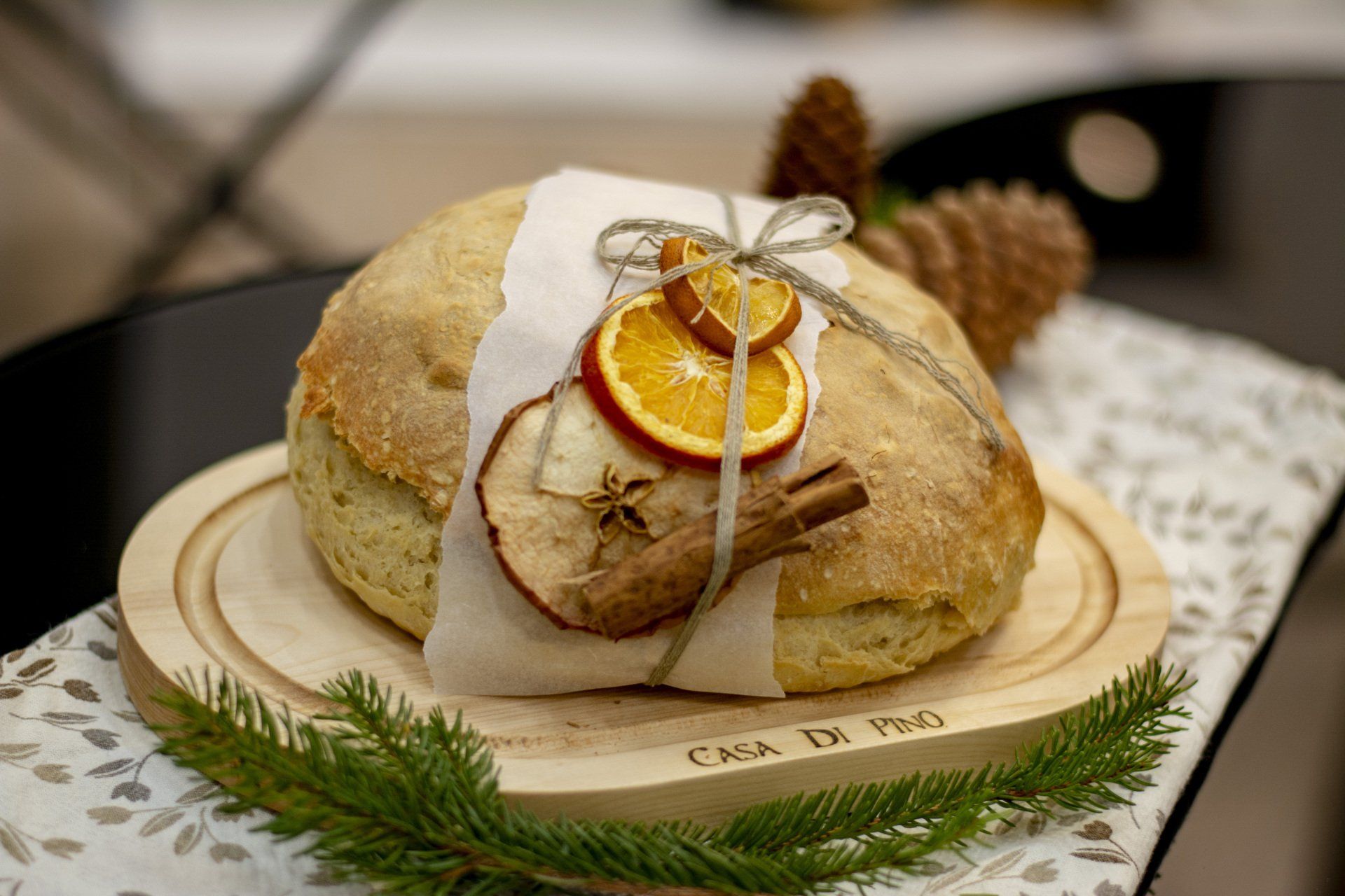 A loaf of bread is wrapped in wax paper and sitting on a wooden cutting board.