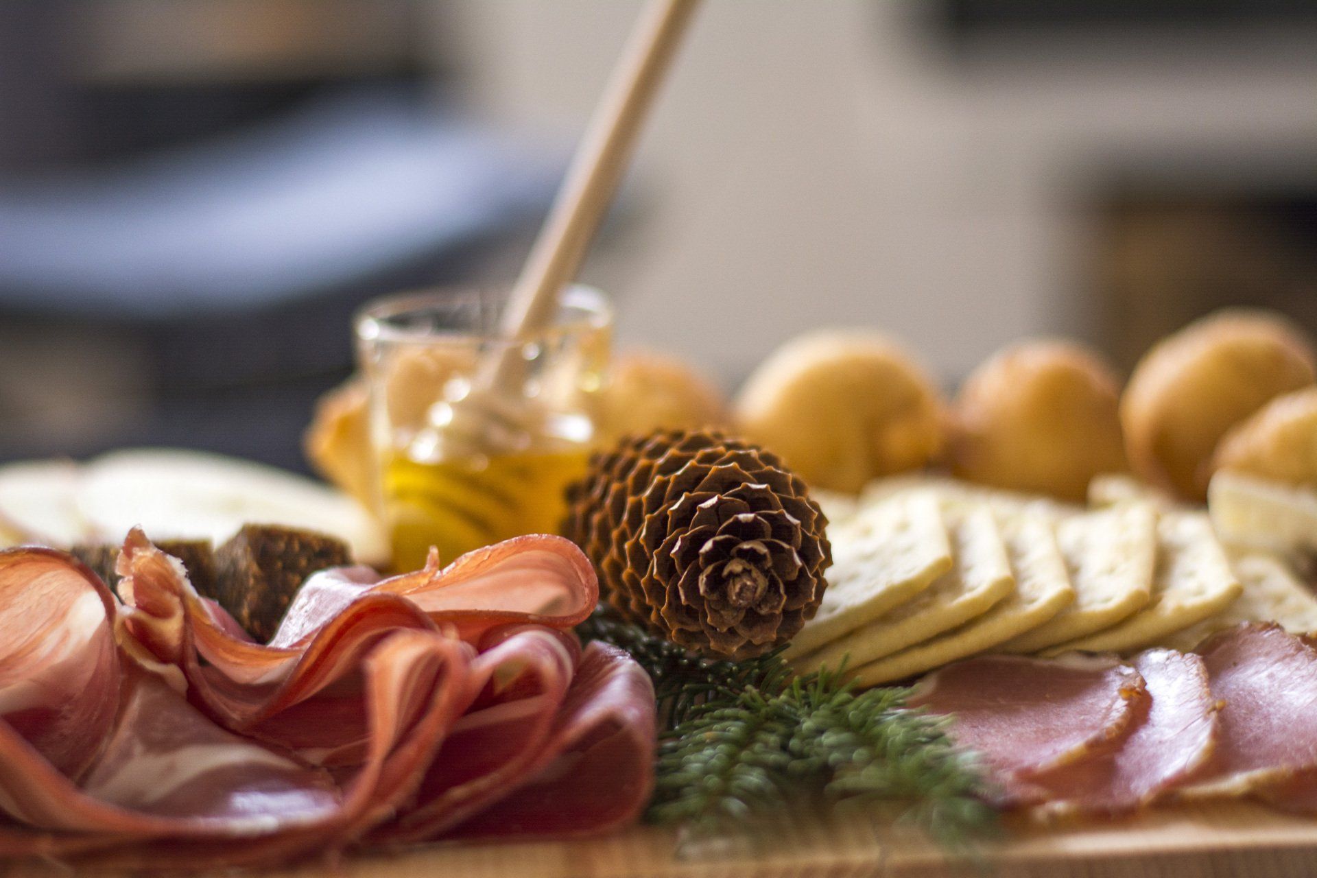 A wooden cutting board topped with meat, cheese, honey and a pinecone.