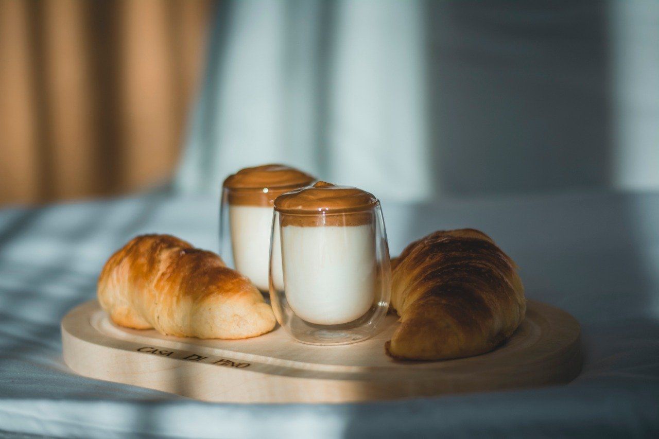 Two croissants and two glasses of milk on a wooden cutting board.