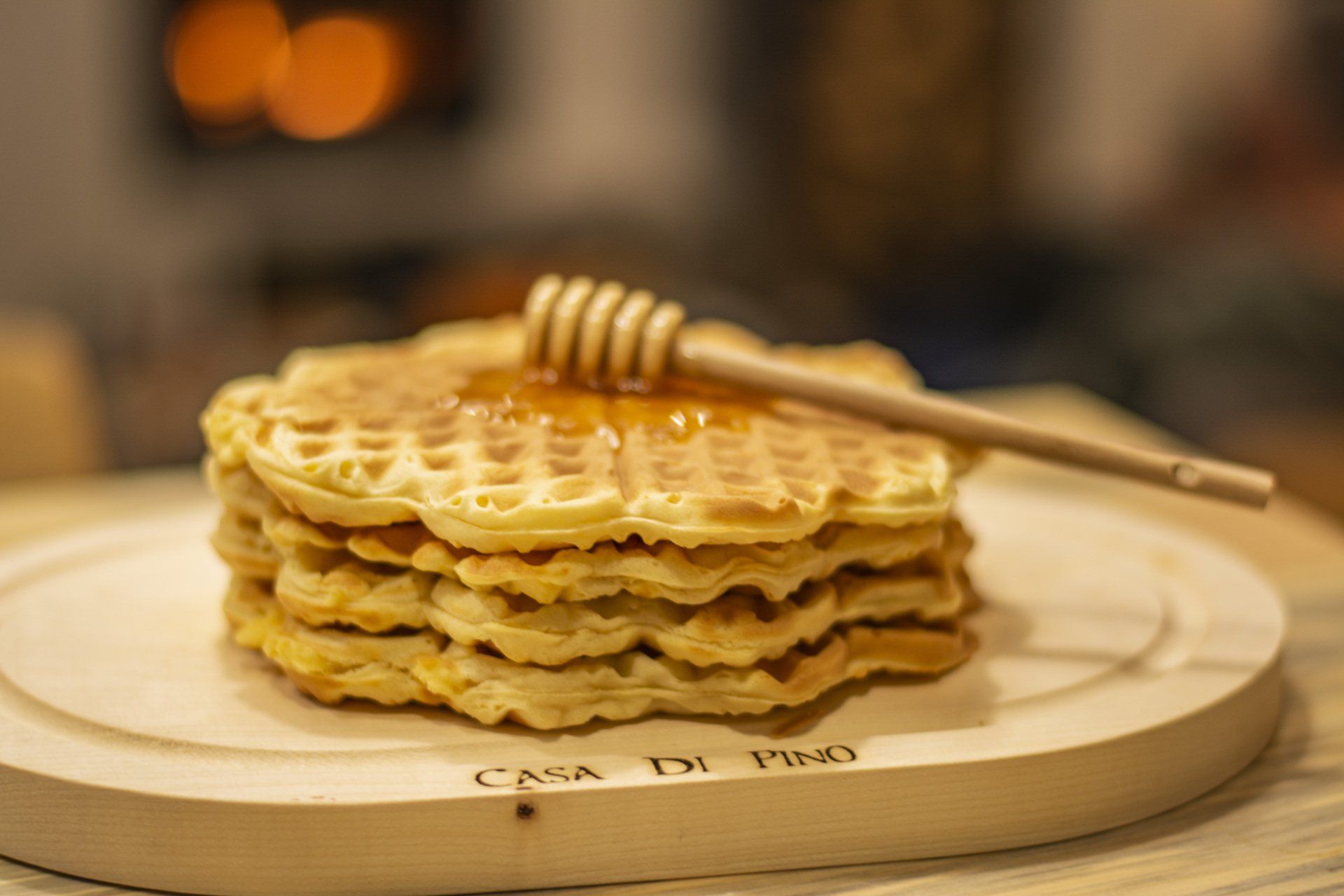 A stack of waffles with honey on a wooden cutting board.