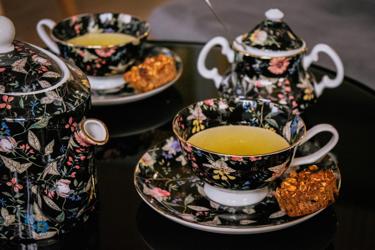 A cup of tea is sitting on a saucer next to a teapot and sugar bowl.