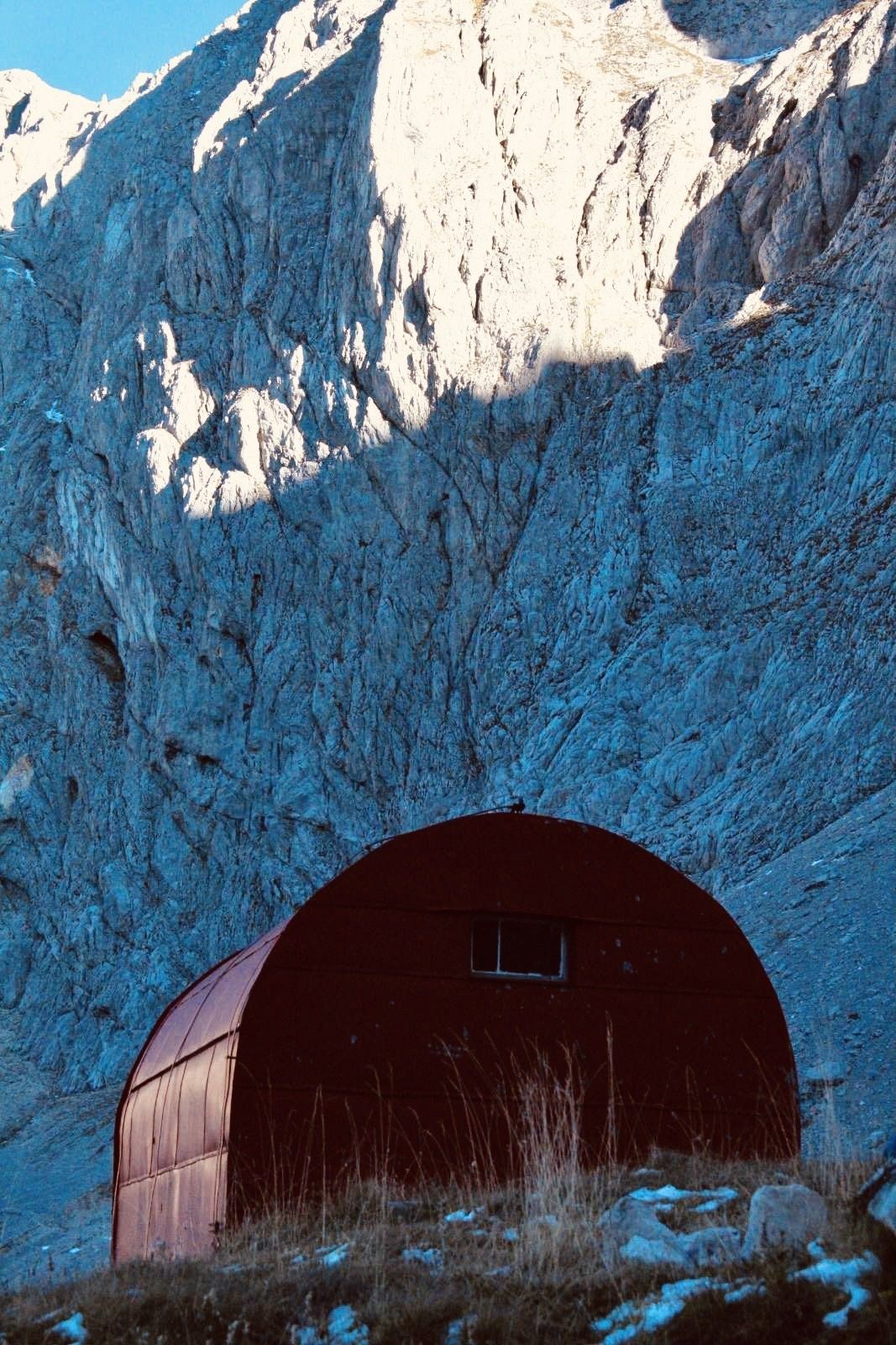 A small red building is sitting in the middle of a snowy mountain.