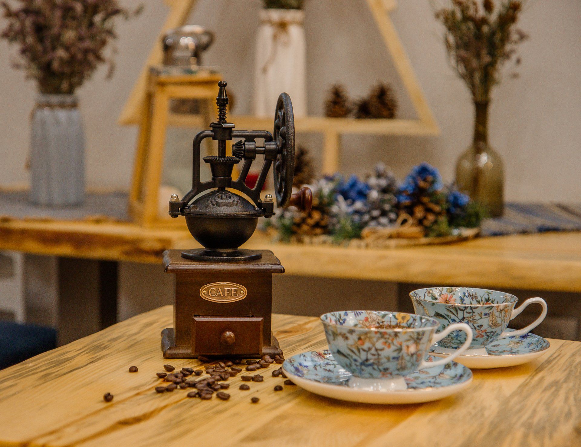 A coffee grinder is sitting on a wooden table next to two cups and saucers.