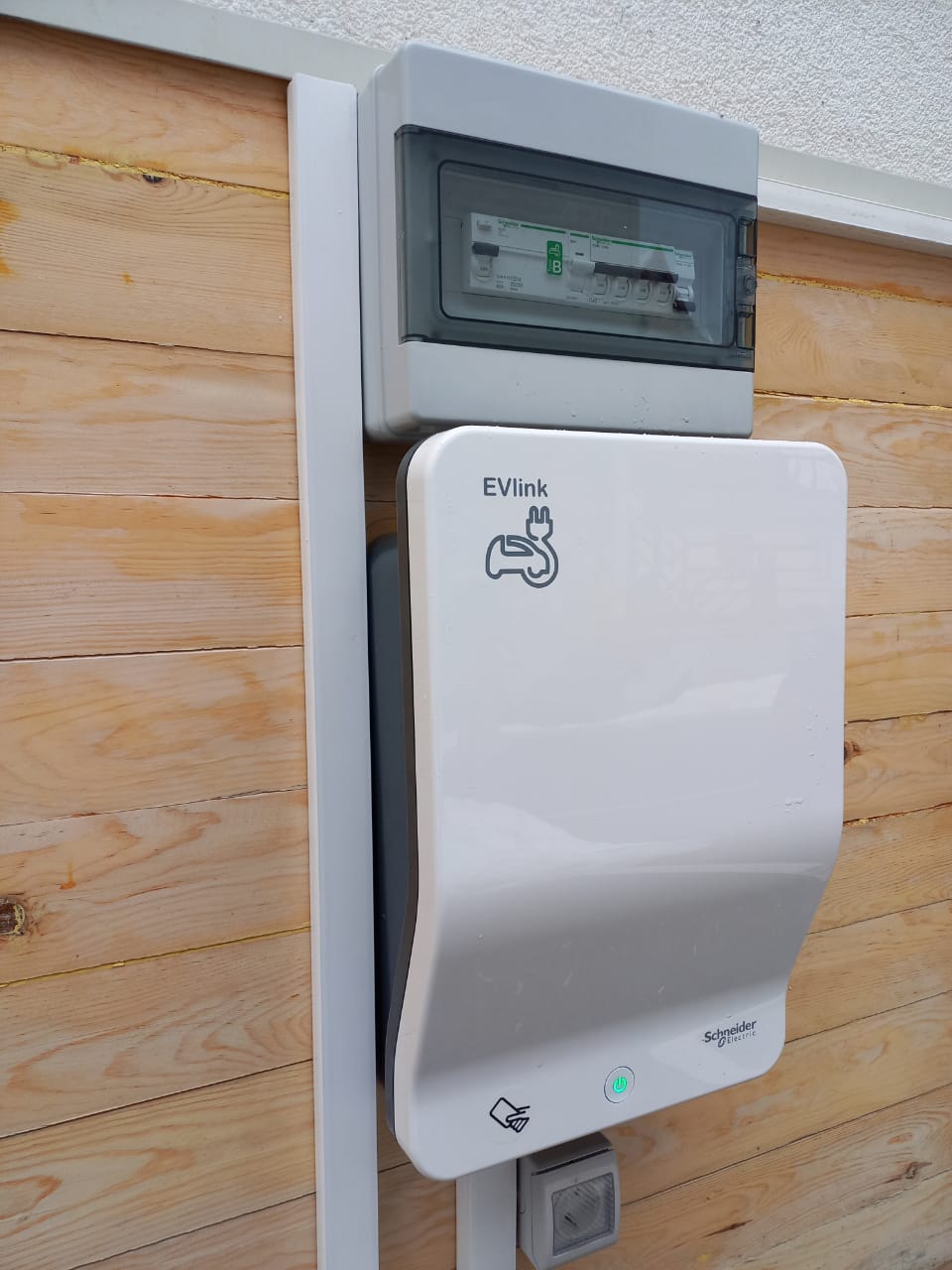 A white electric vehicle charging device is sitting on top of a wooden wall.