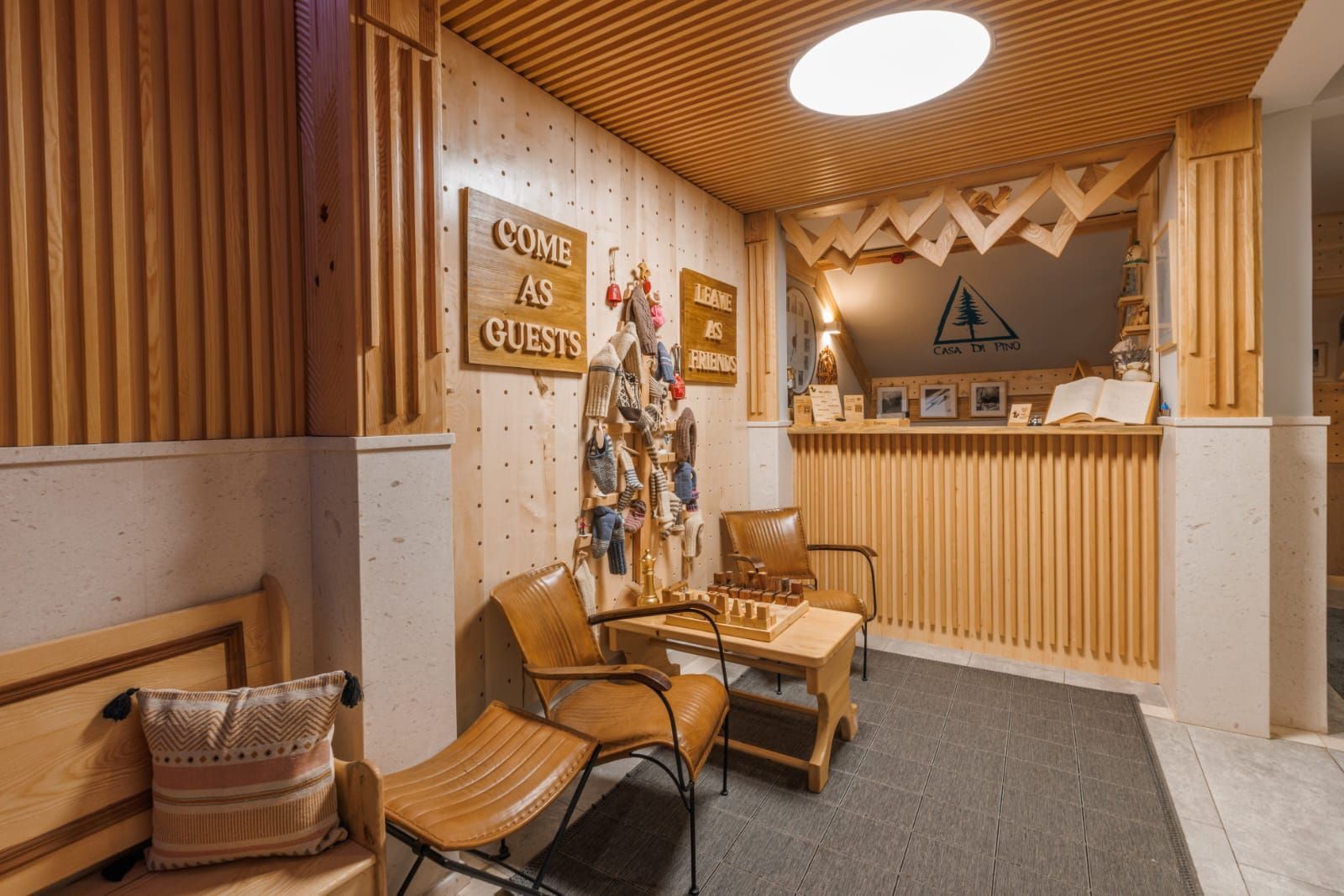 A hotel lobby with a front desk made of wood, chairs, a table and wooden details, and a sign that says, 