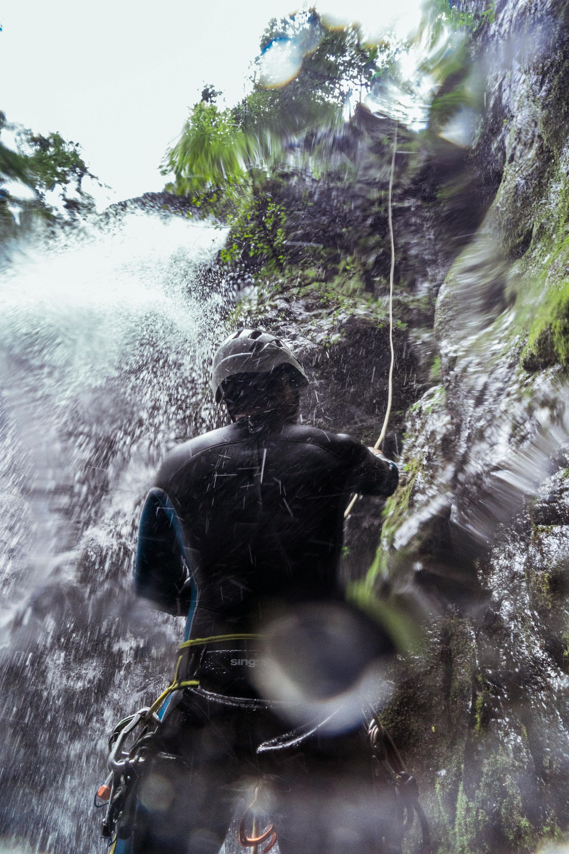 Person rappelling down a waterfall, wearing a wetsuit, with water cascading around them.