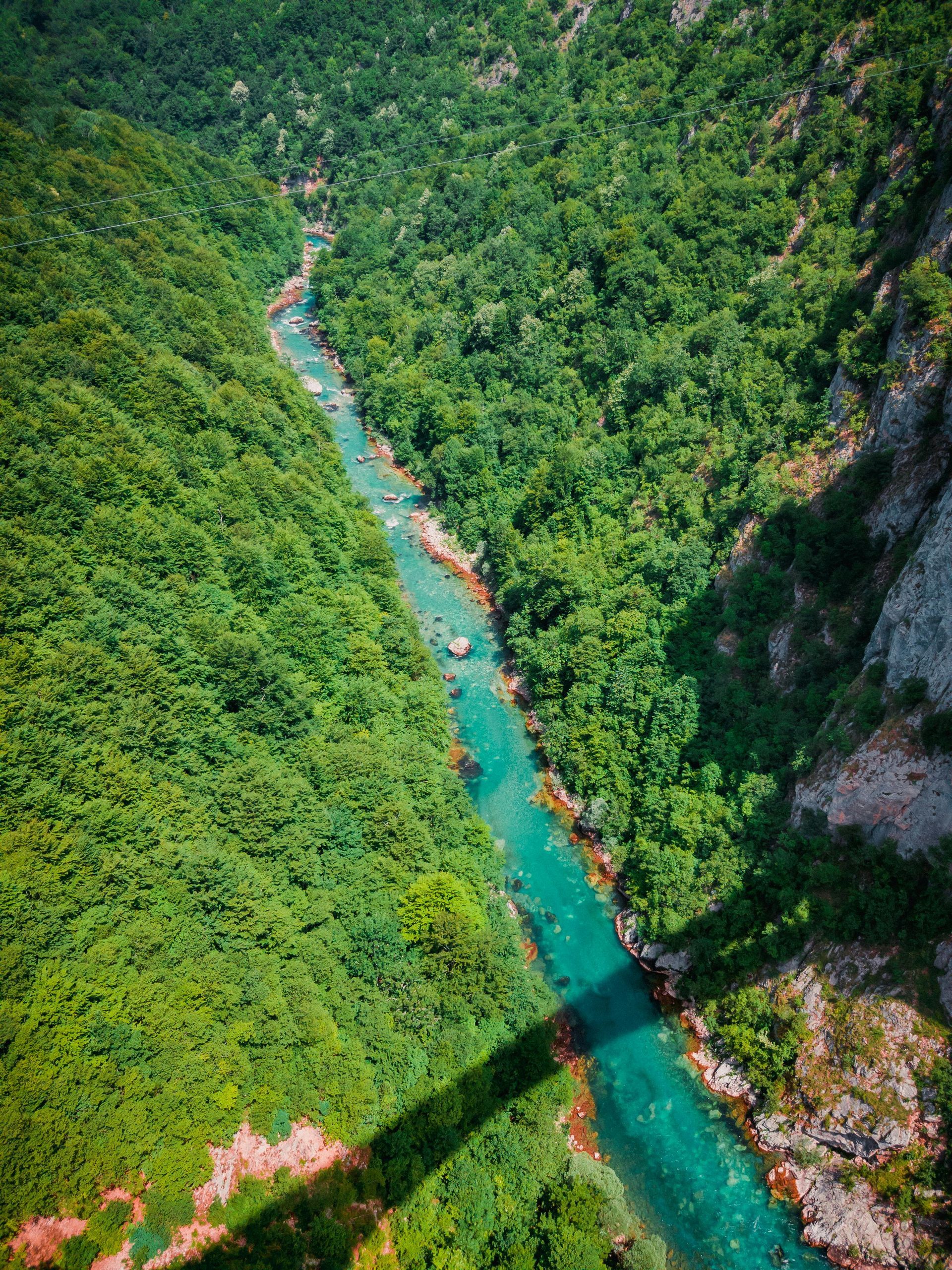 A turquoise river flows through a lush green canyon, with a bridge shadow visible.