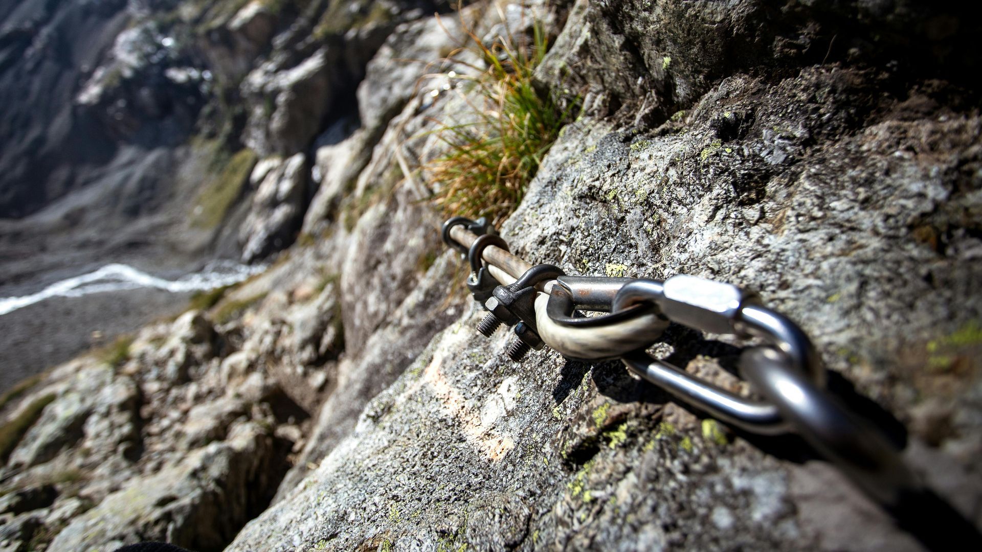 Close-up of metal safety carabiner and chain attached to a rock face on a mountain trail.