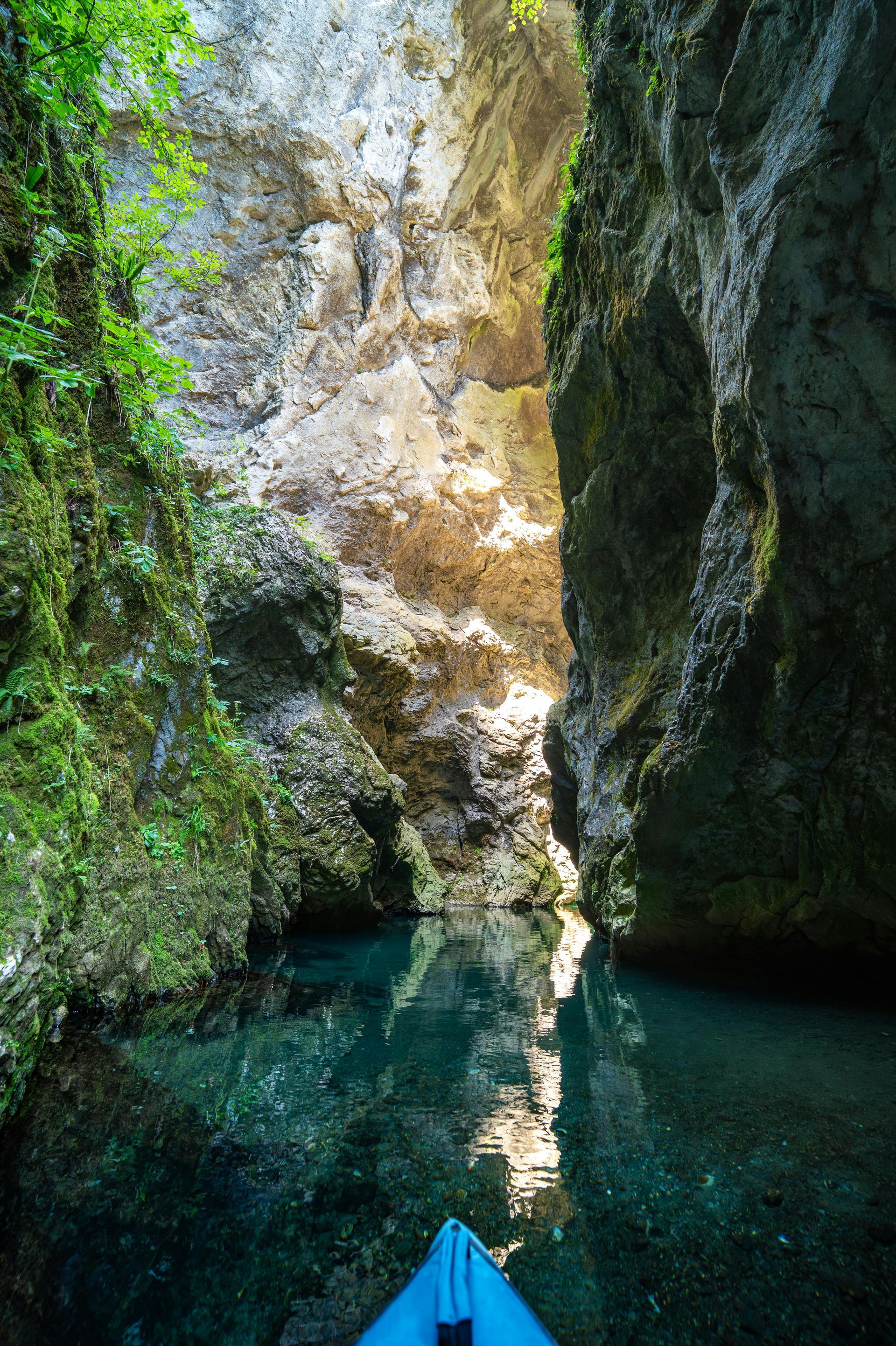 Kayaker in a narrow gorge with clear turquoise water. Sunlight streams in, illuminating the light-colored rock walls.