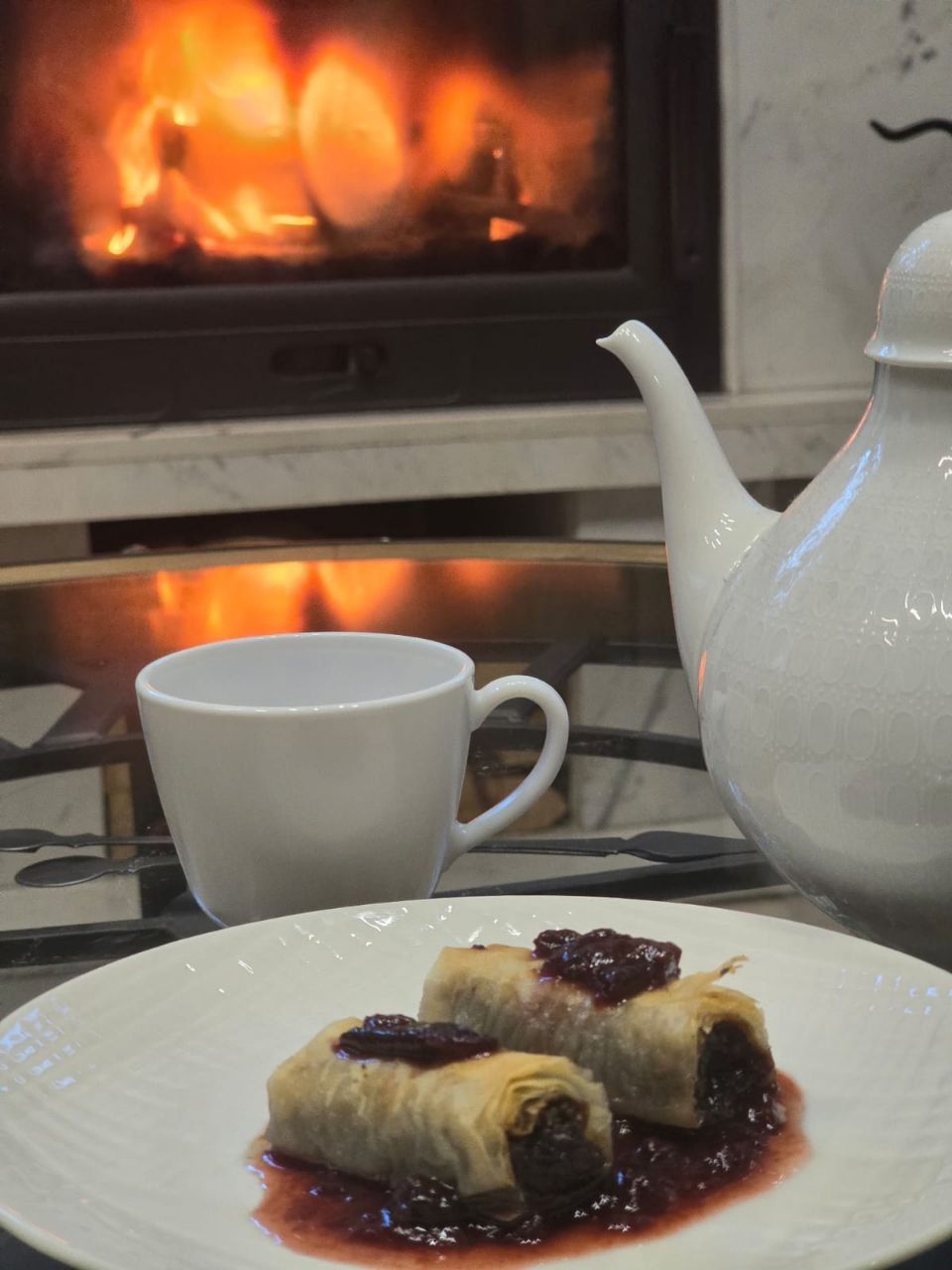 A plate with cake and a cup of tea in front of a fireplace