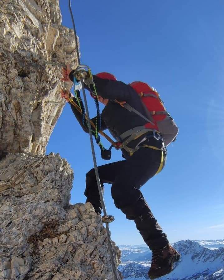 Person climbing a steep, rocky mountainside, using a via ferrata system.