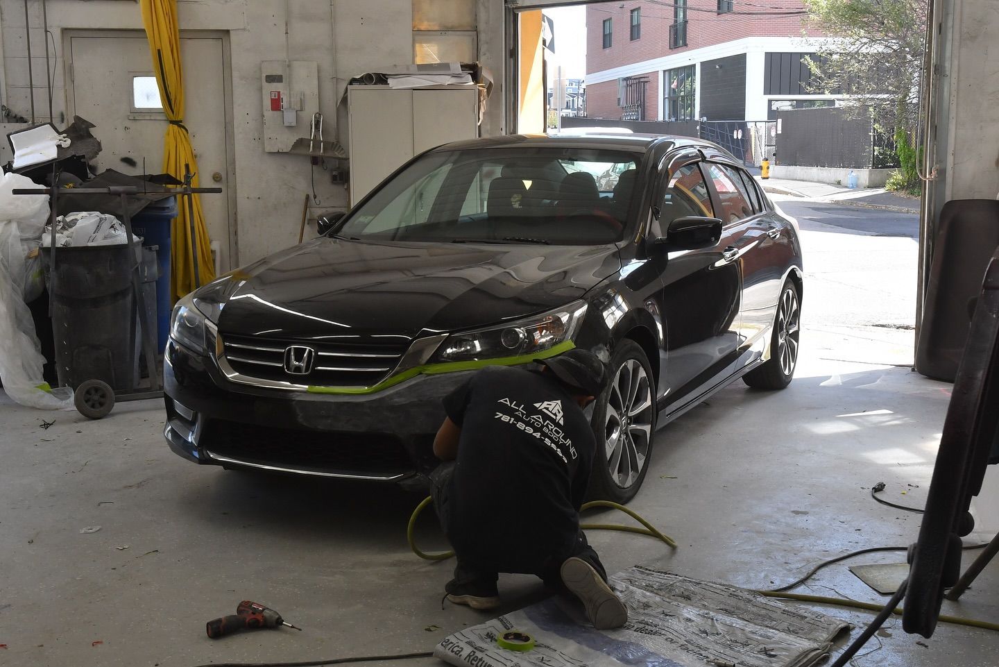 Person working on a black car in a garage, applying tape.
