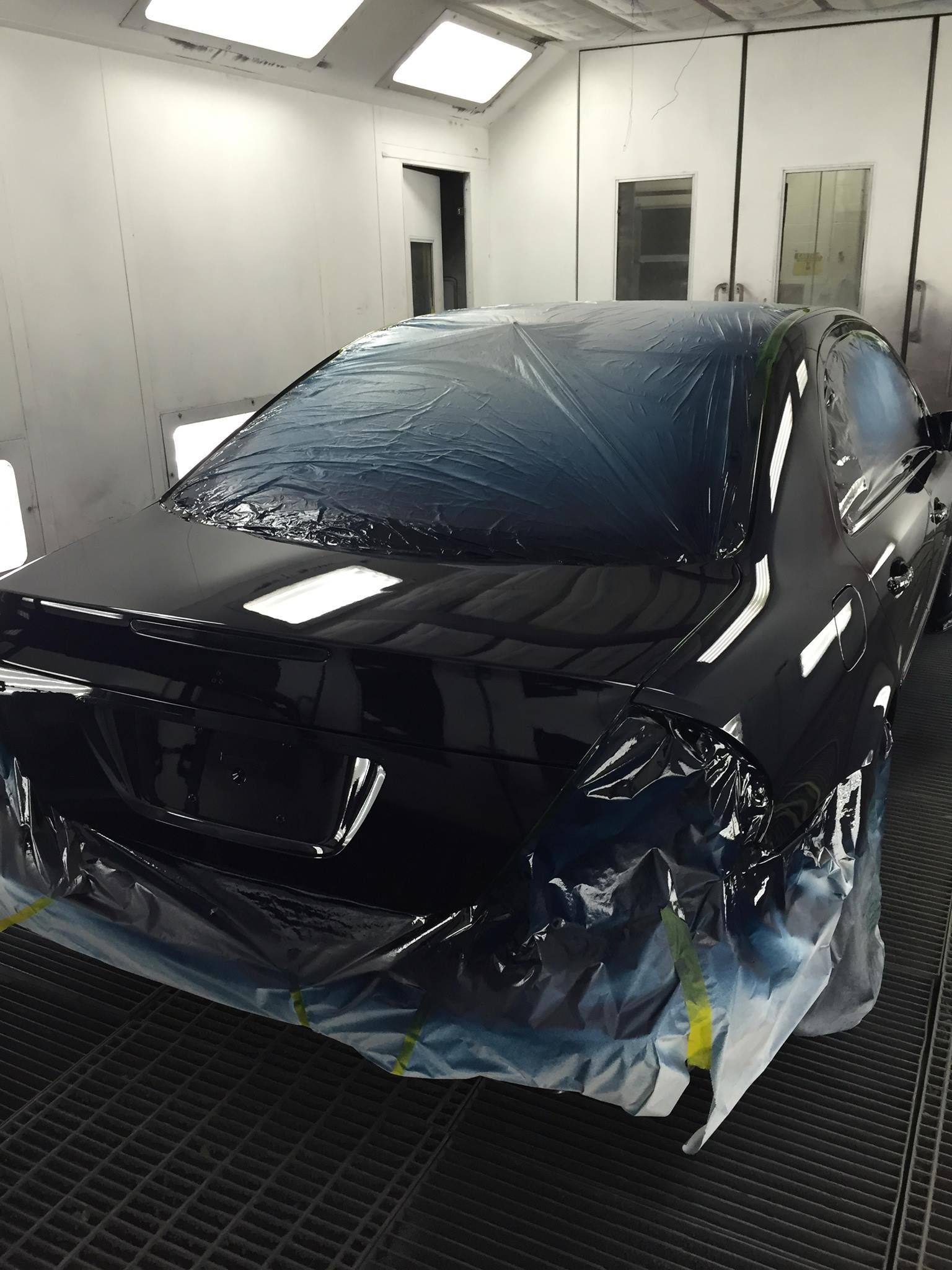 Black car in a paint booth, covered with protective plastic, being repainted.