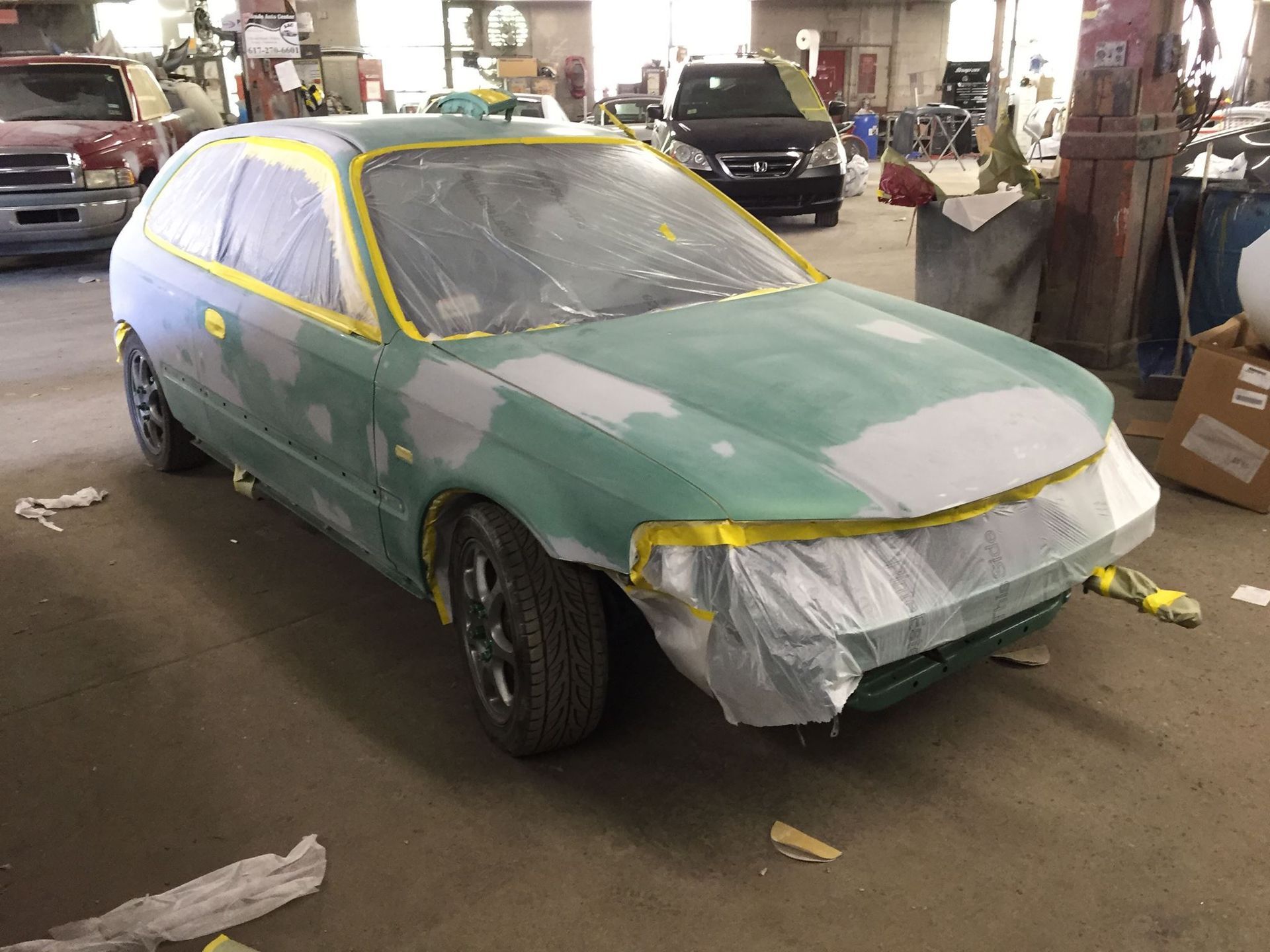 Green car, body work, taped windows and panels, in a repair shop.