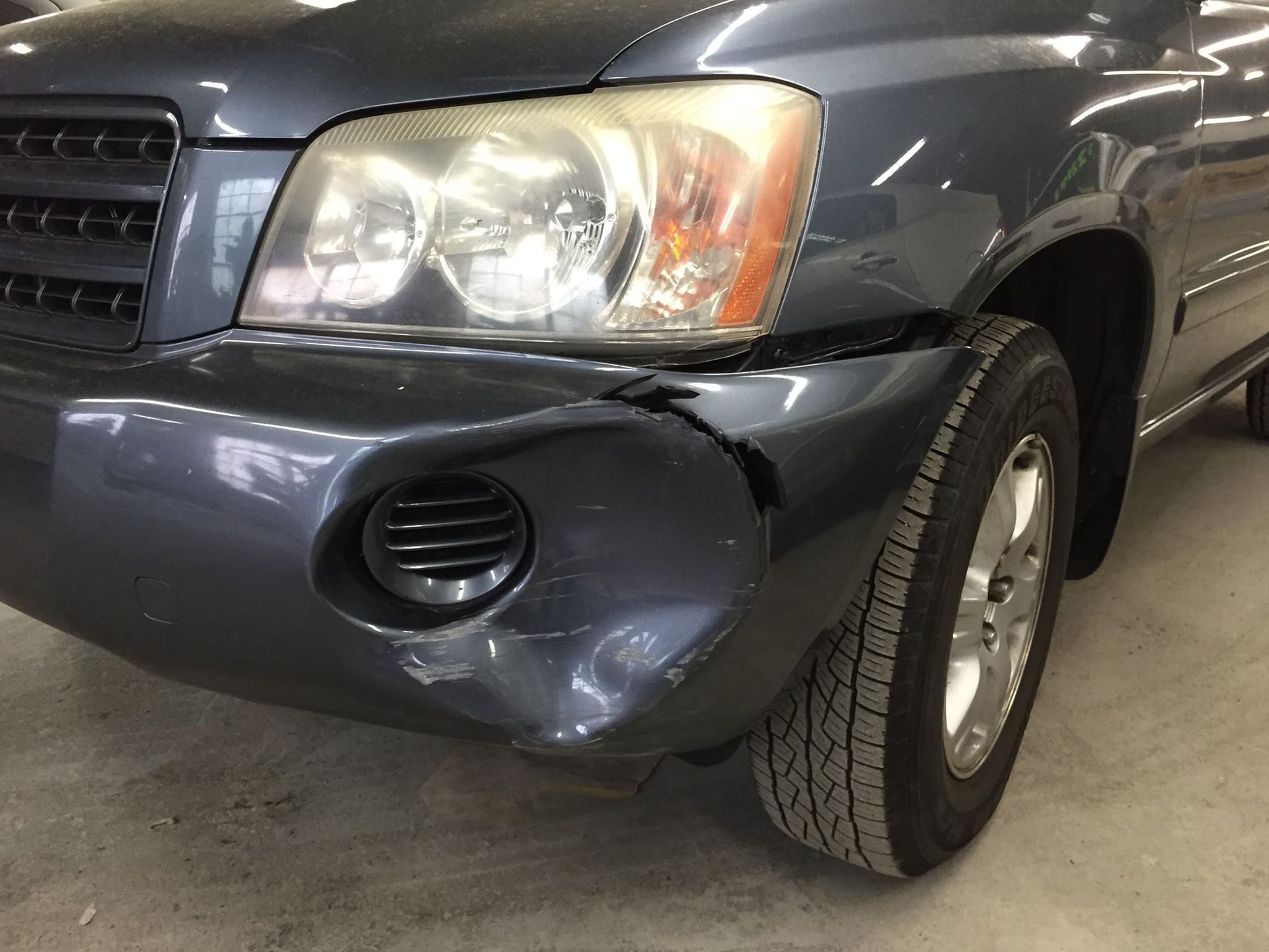 Damaged dark blue SUV front bumper with a visible dent and crack near the headlight and fog light.