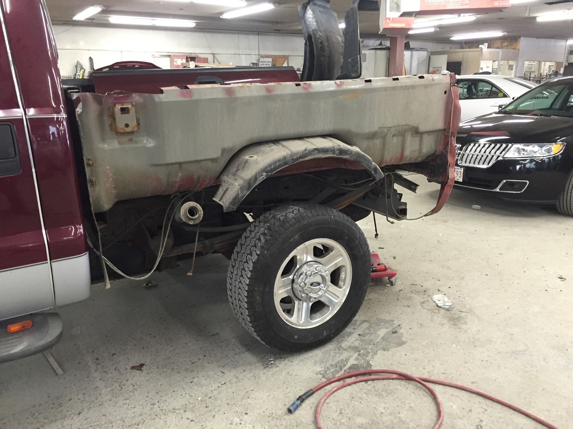 Truck bed undergoing repair, revealing the truck's frame. The wheel well is visible with a mounted tire.
