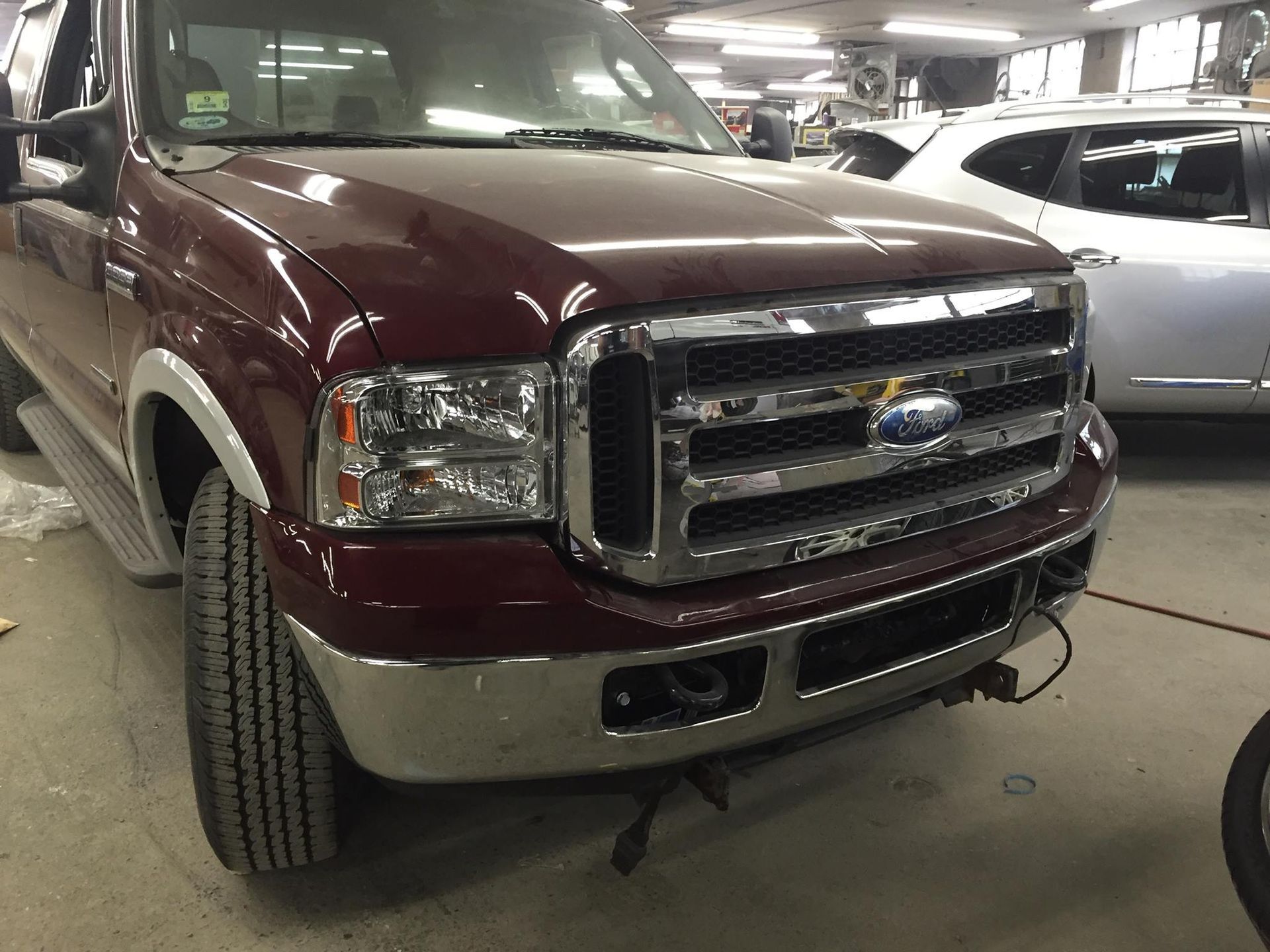 Burgundy Ford truck in a garage; chrome grill and bumper, gray tire.