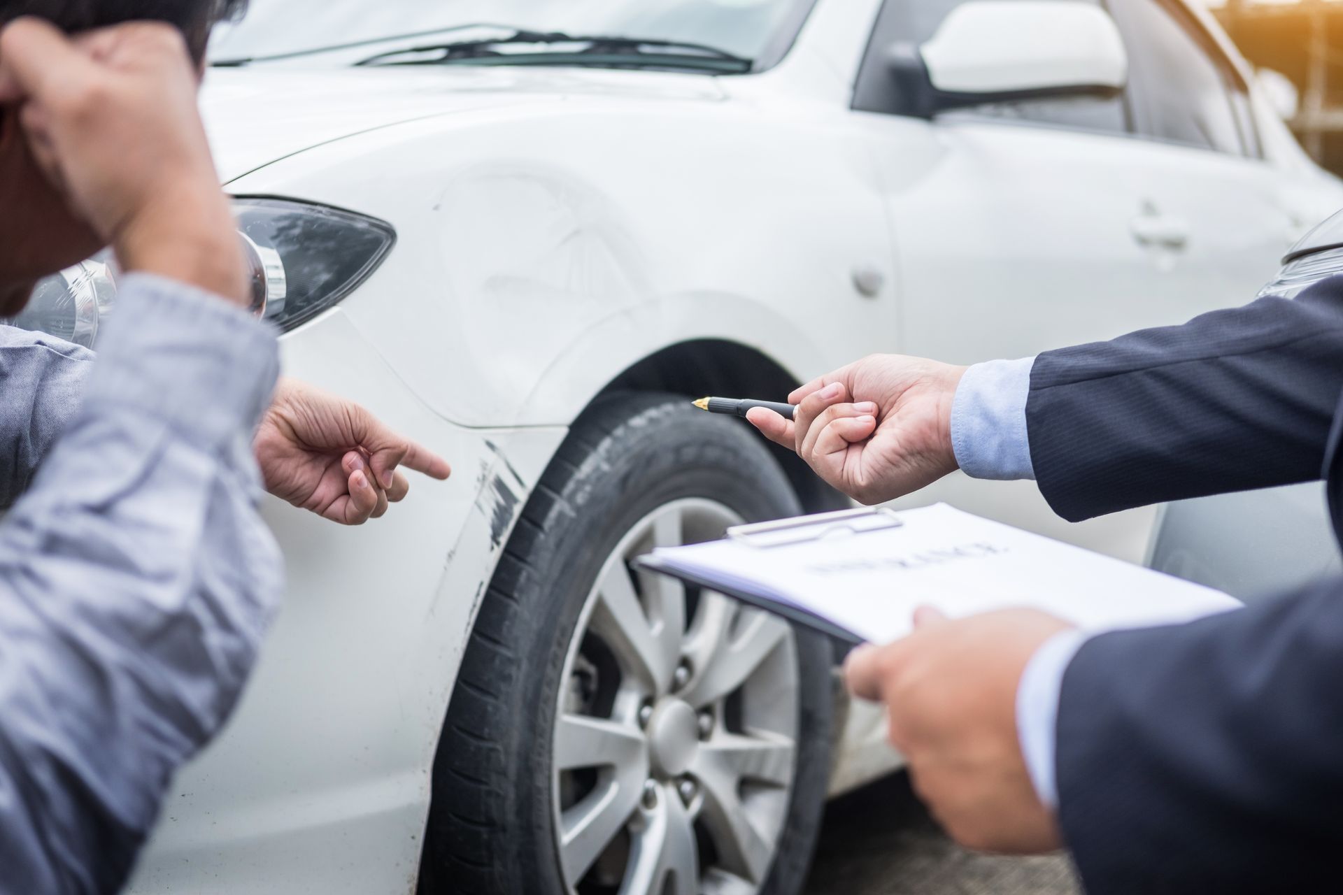 Man points at car damage while another holds clipboard and pen. White car.