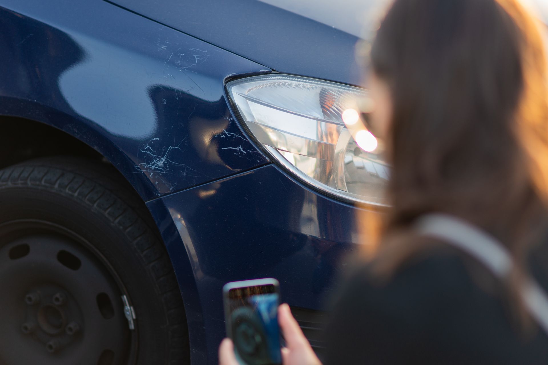 Person taking photo of damaged blue car fender with a smartphone.