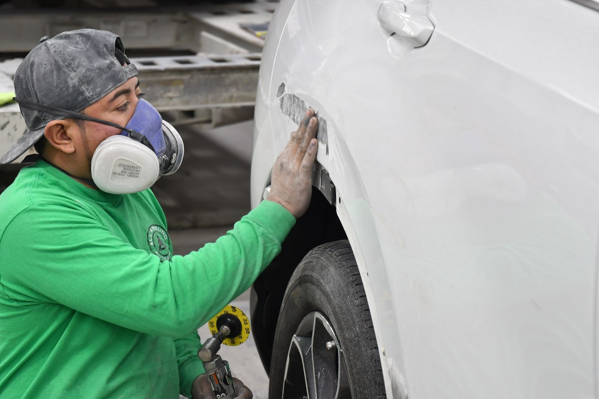 Person in respirator sanding white car body in a garage.