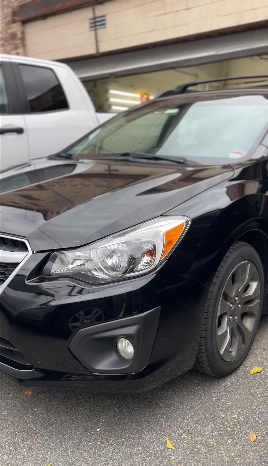 Black Subaru Impreza parked on a street in front of a building with a white truck to its left.