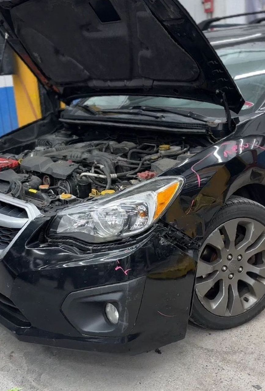 Black Subaru with hood open, showing engine and front-end damage.