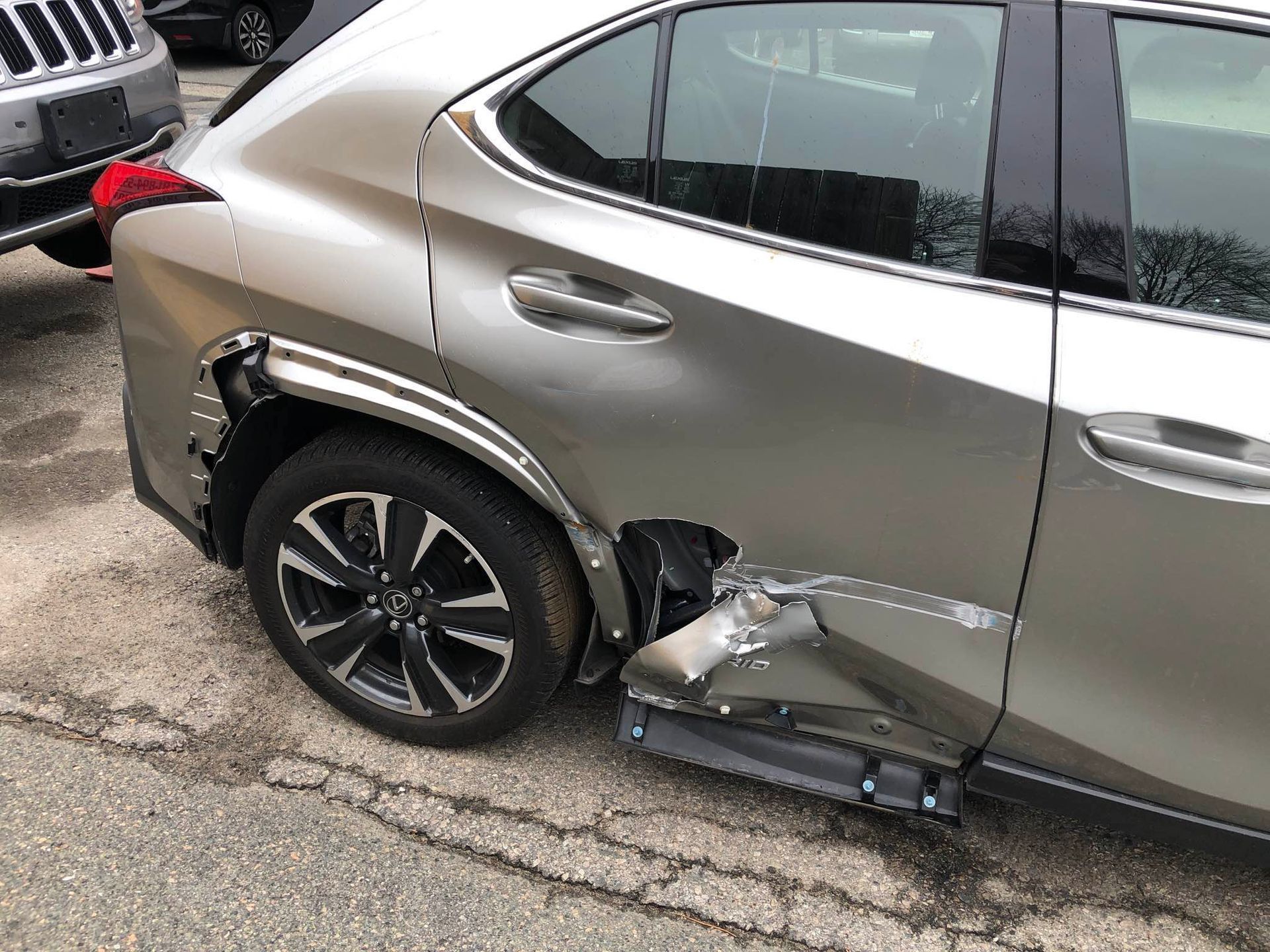 Damaged silver Lexus SUV, rear quarter panel dented and torn, parked on asphalt.