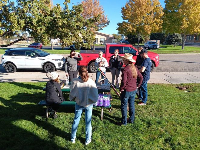 A group of people are standing around a picnic table in a park.