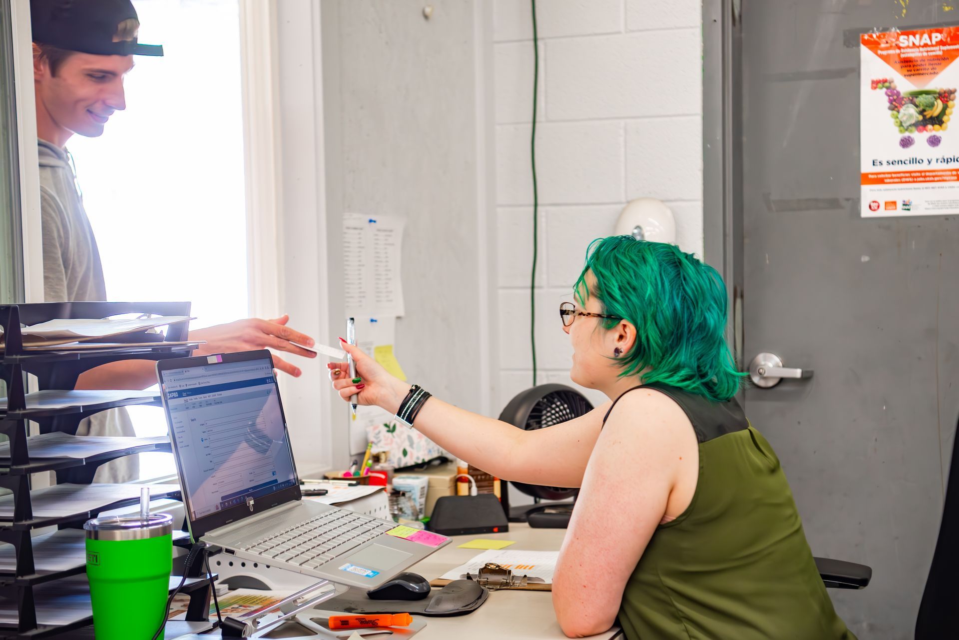 A woman with green hair is sitting at a desk in front of a laptop computer.