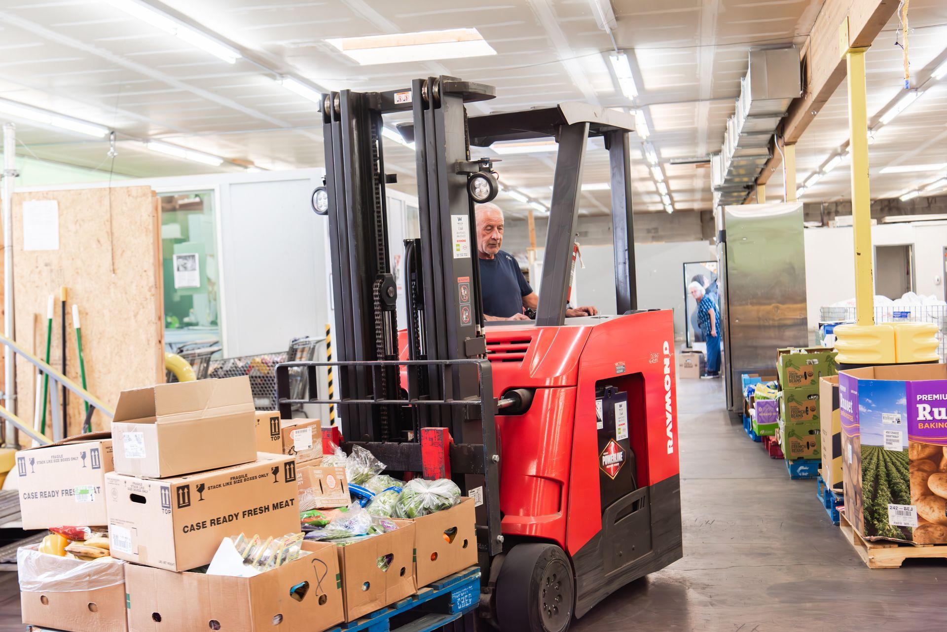 A man is driving a red forklift in a warehouse filled with boxes.