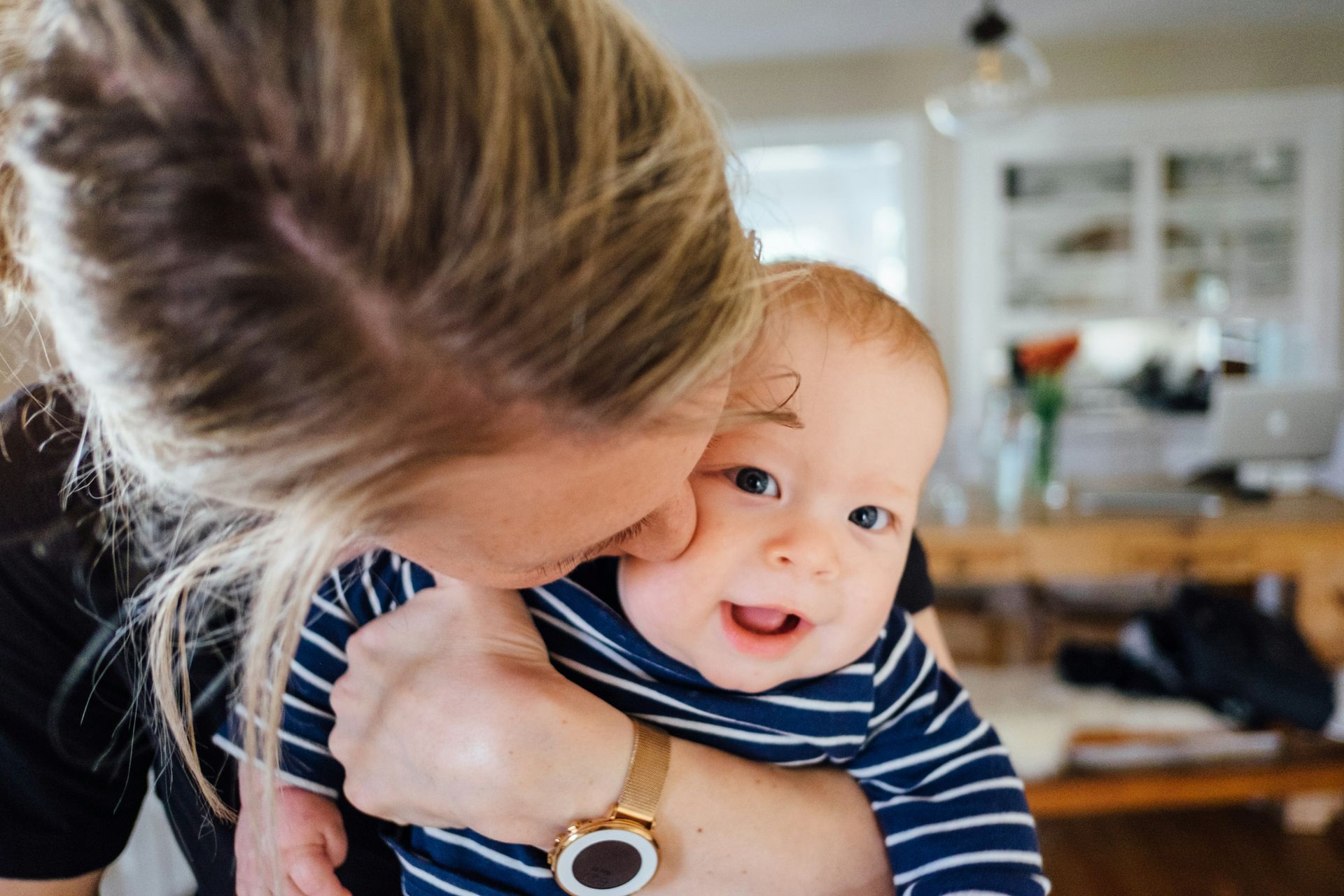 A woman is holding a baby in her arms and kissing it on the cheek.