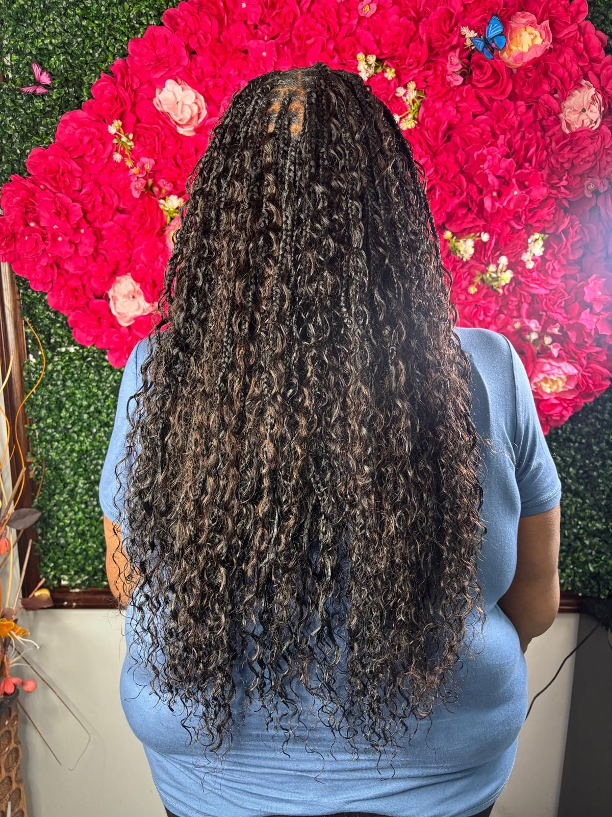 Long, dark, curly hair falling down the back of a person wearing a blue shirt against a backdrop of red flowers.