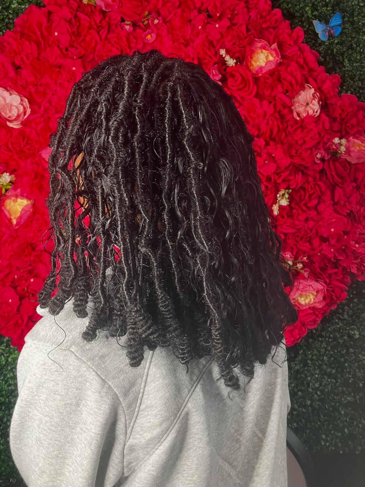 Shoulder-length, dark, textured locs with curled ends in front of a red floral background.